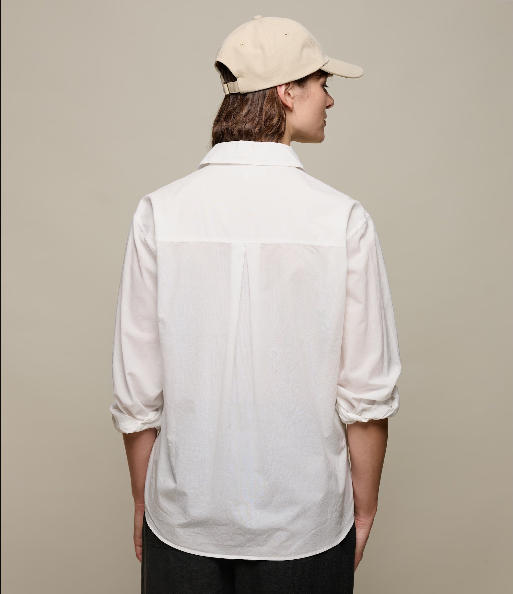 Person wearing a white linen shirt and beige cap on a plain background