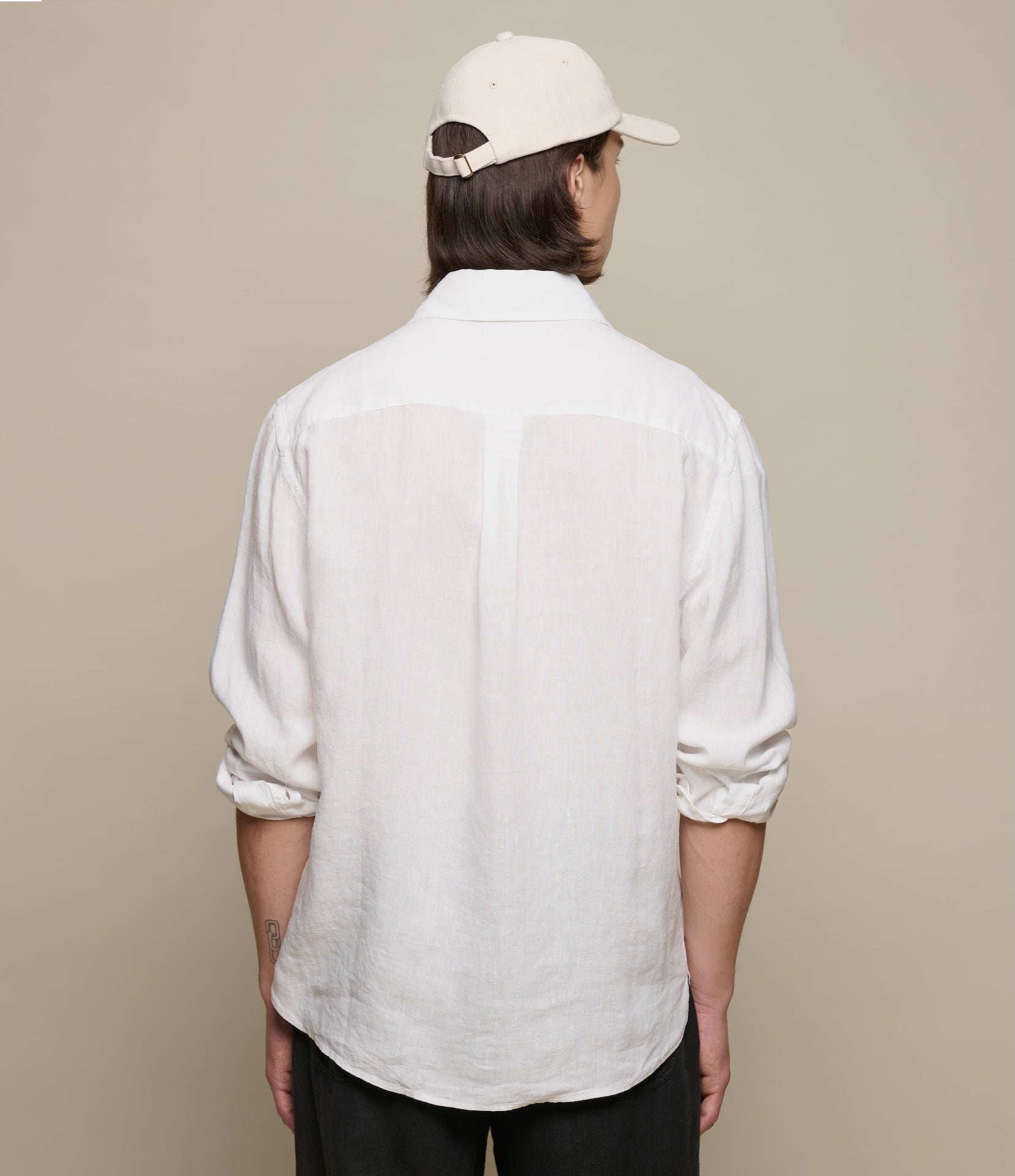 Person wearing a white linen shirt and beige cap from behind on a beige background