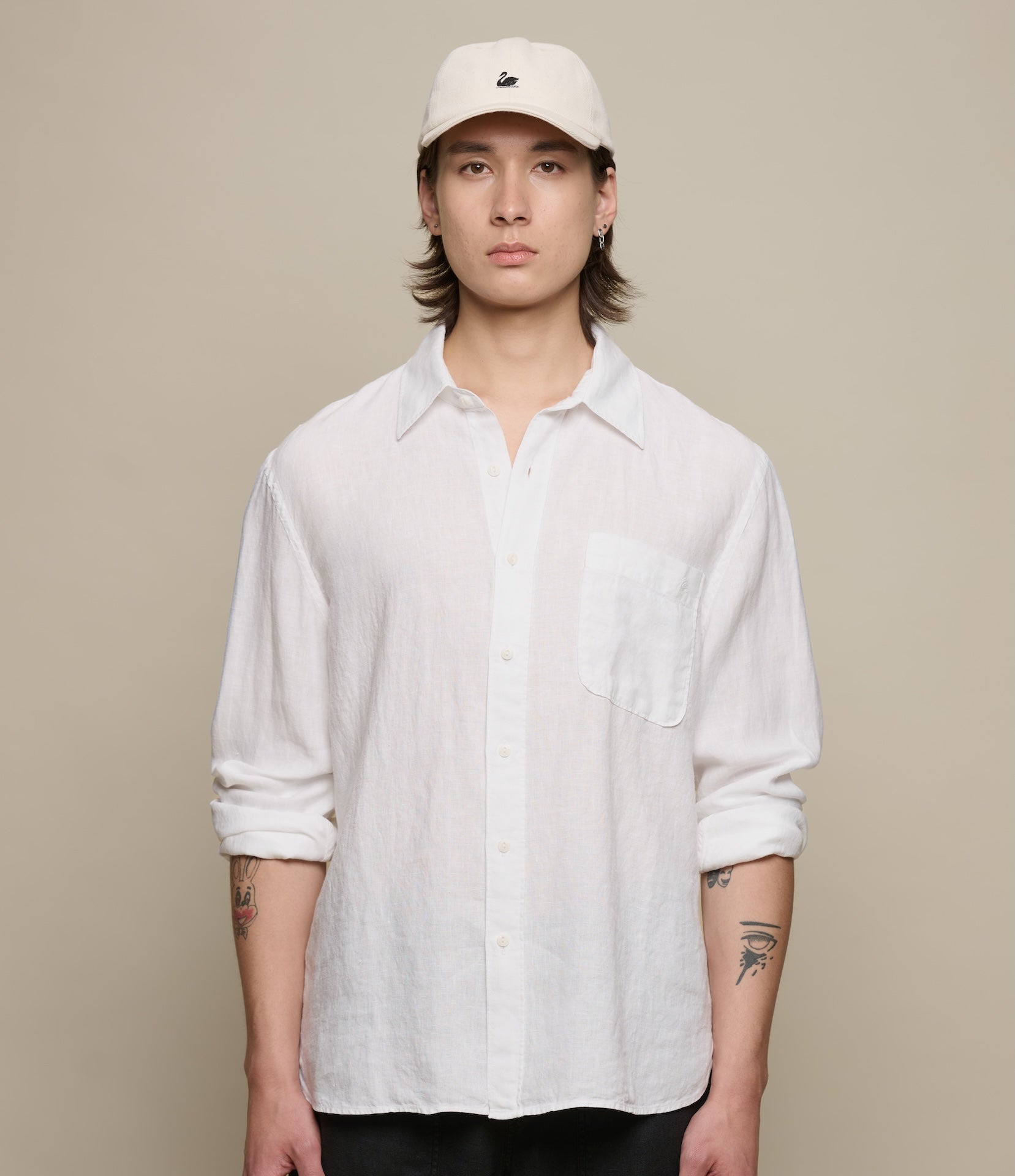 Person wearing a white linen shirt and cap on a beige background
