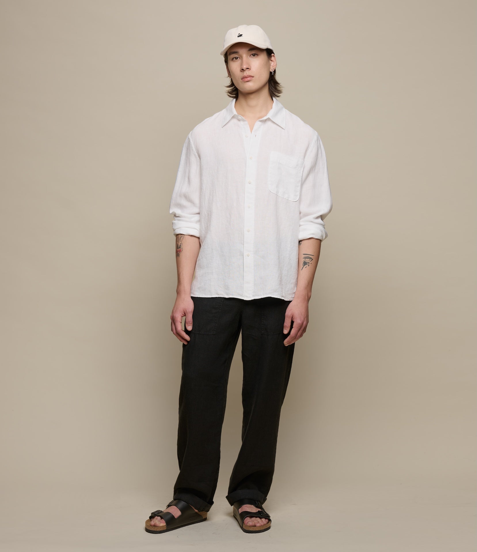 Person wearing a white linen shirt and black linen pants against a beige background