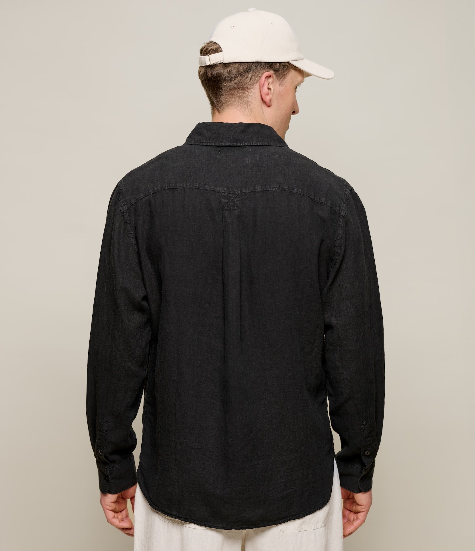 Man wearing a black shirt and white cap from behind on a plain background