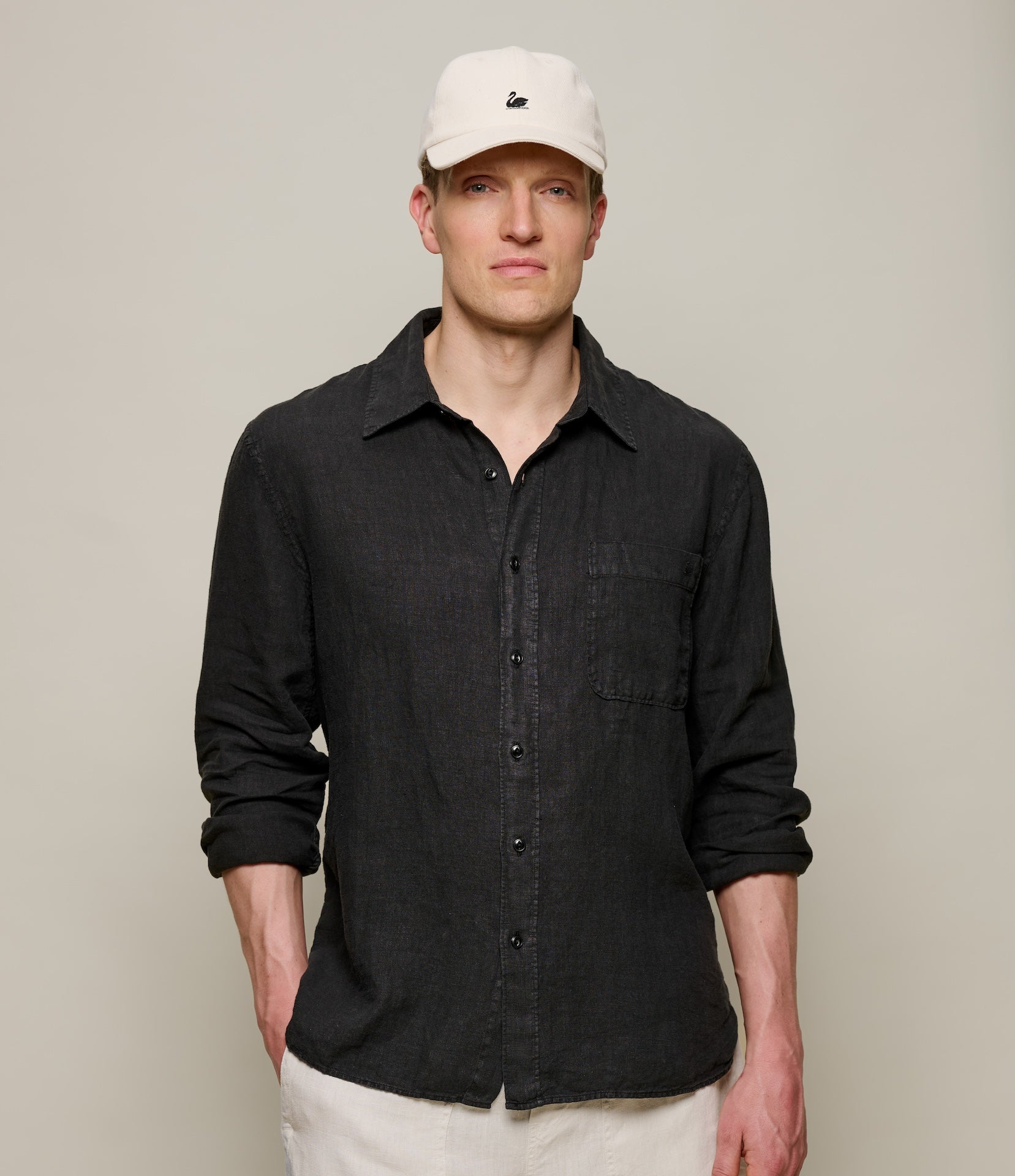 Man wearing a black button-up linen shirt and white cap against a plain background