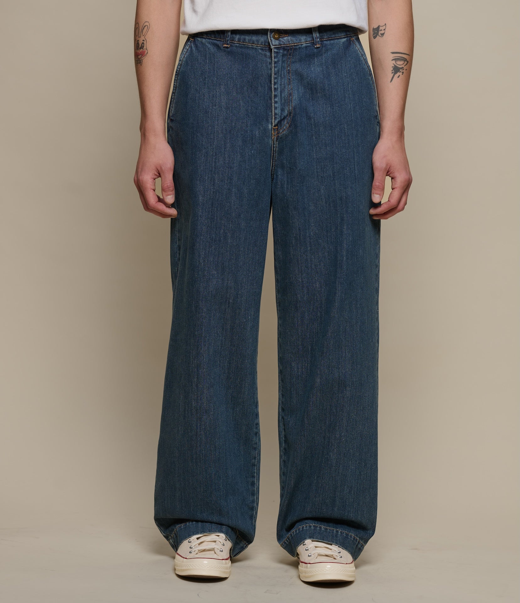 Person wearing blue jeans and white sneakers on a beige background