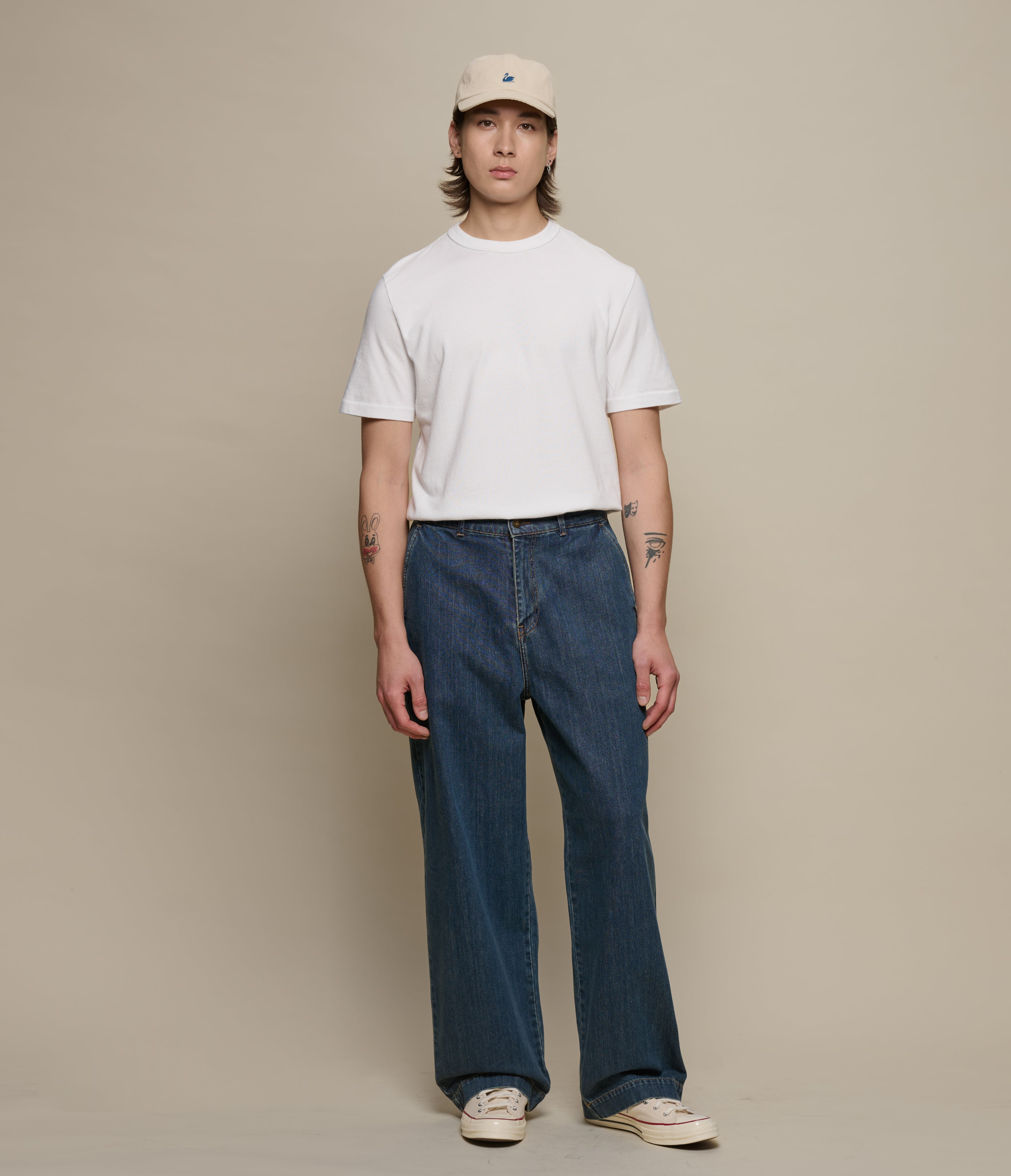 Person wearing a white t-shirt and blue jeans against a beige background