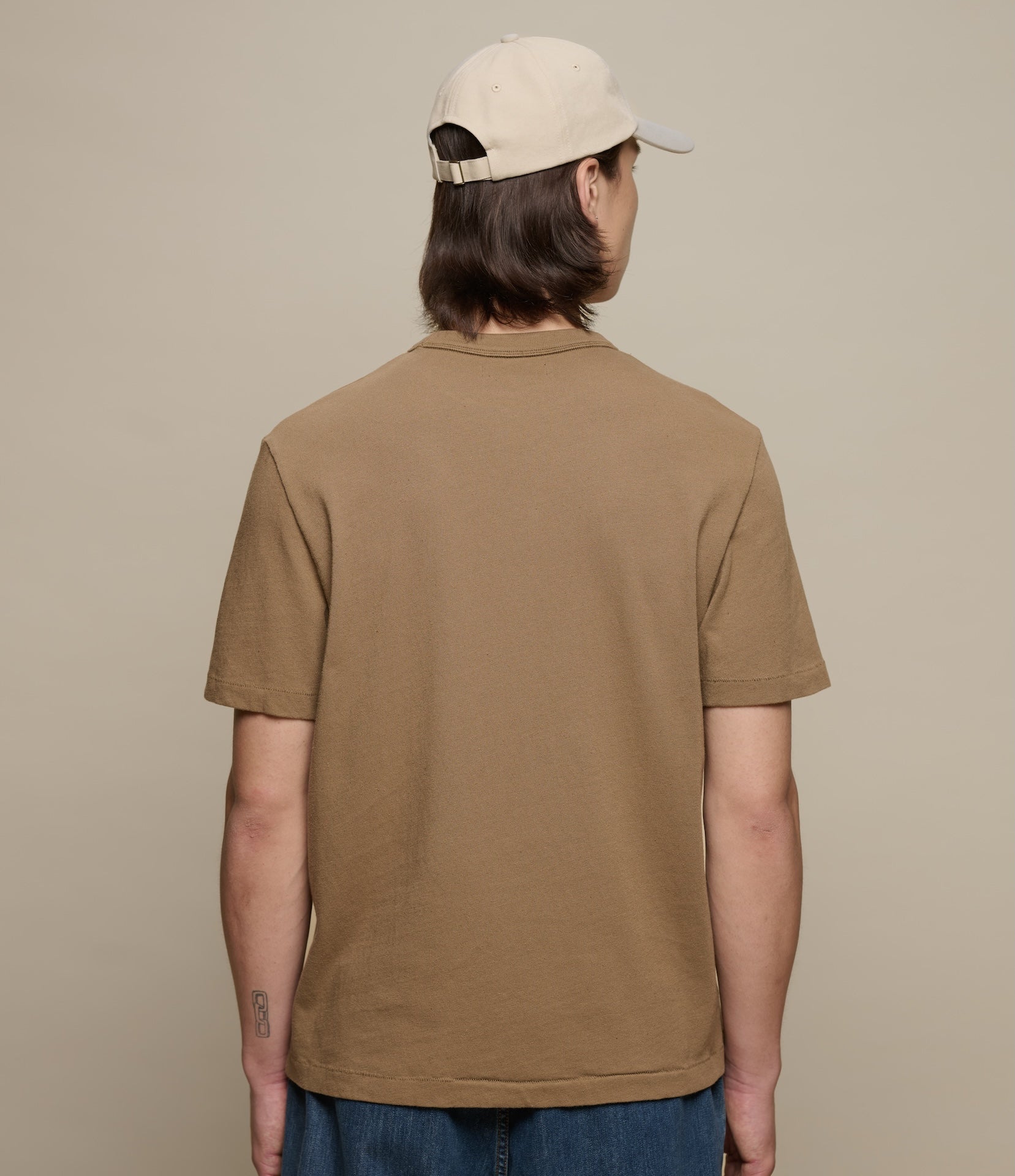 Person wearing a brown t-shirt and beige cap from behind on a beige background