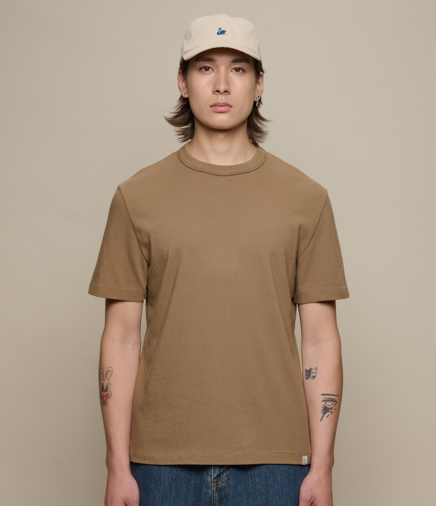 Person wearing a brown authentic jersey t-shirt and beige cap against a beige background