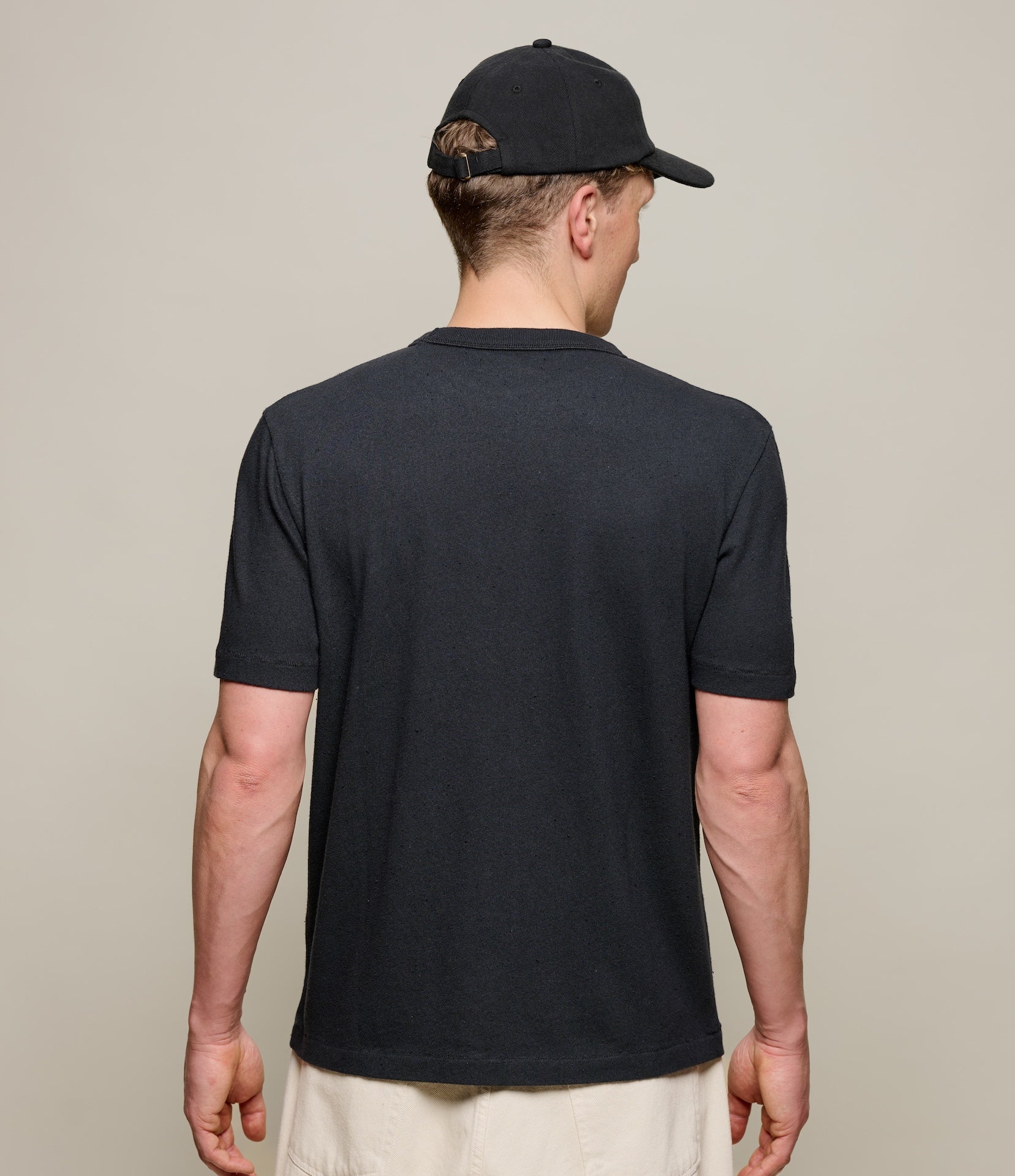 Man wearing a black t-shirt and cap from behind on a beige background