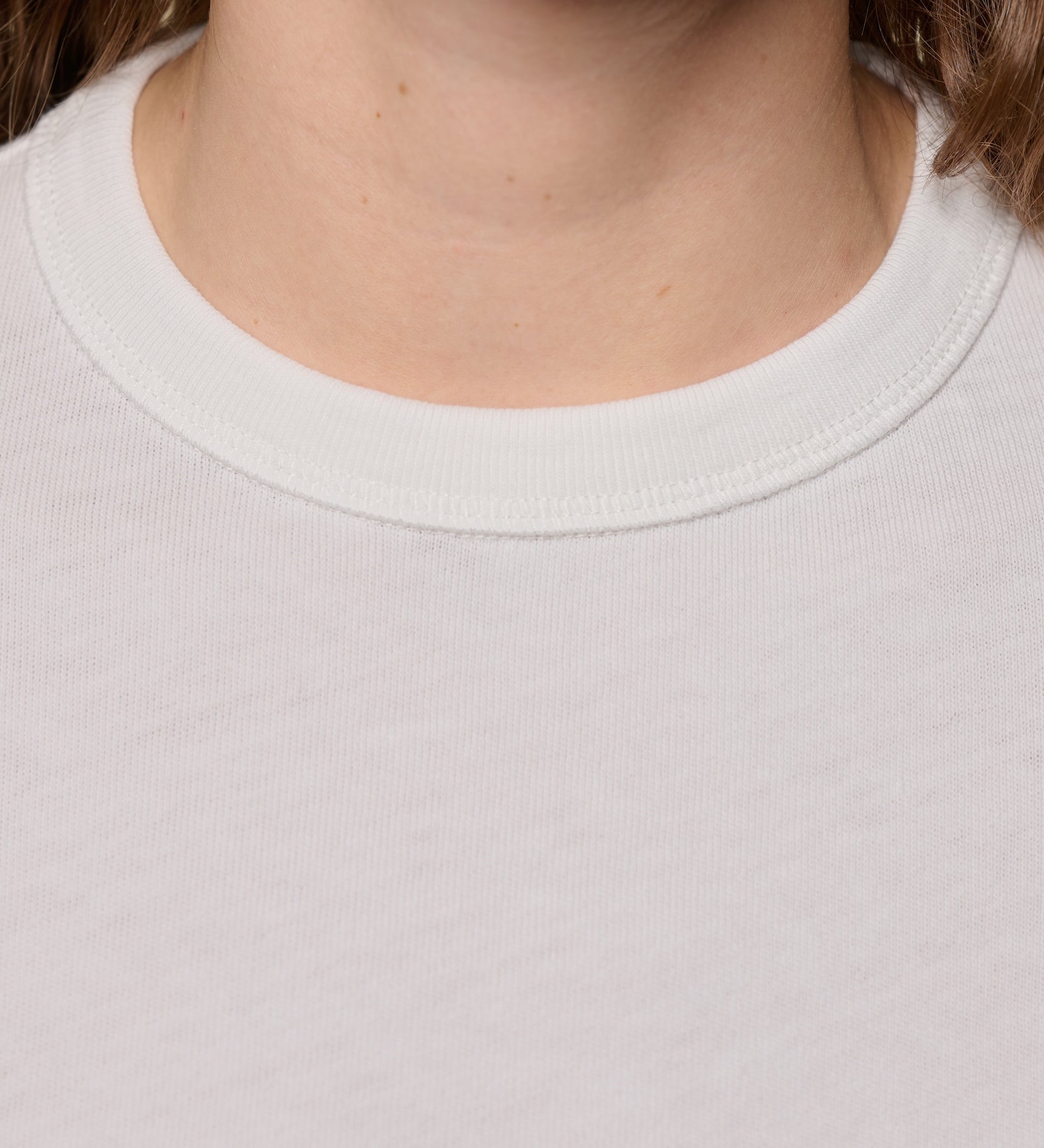 Close-up of a person wearing a plain white t-shirt with a focus on the ribbed neckline.