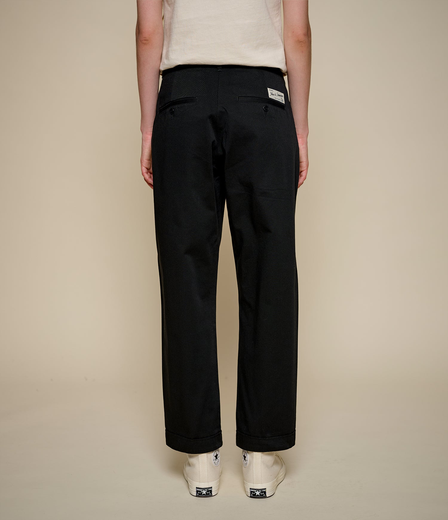 A person shown from the back wearing black wide-leg trousers, a cream sleeveless top, and white sneakers against a plain beige studio background.