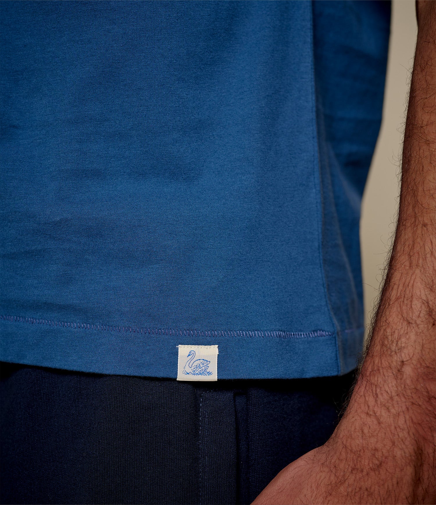 Close-up of a indigo blue T-shirt with a Merz b. Schwanen brand logo on a person wearing it.
