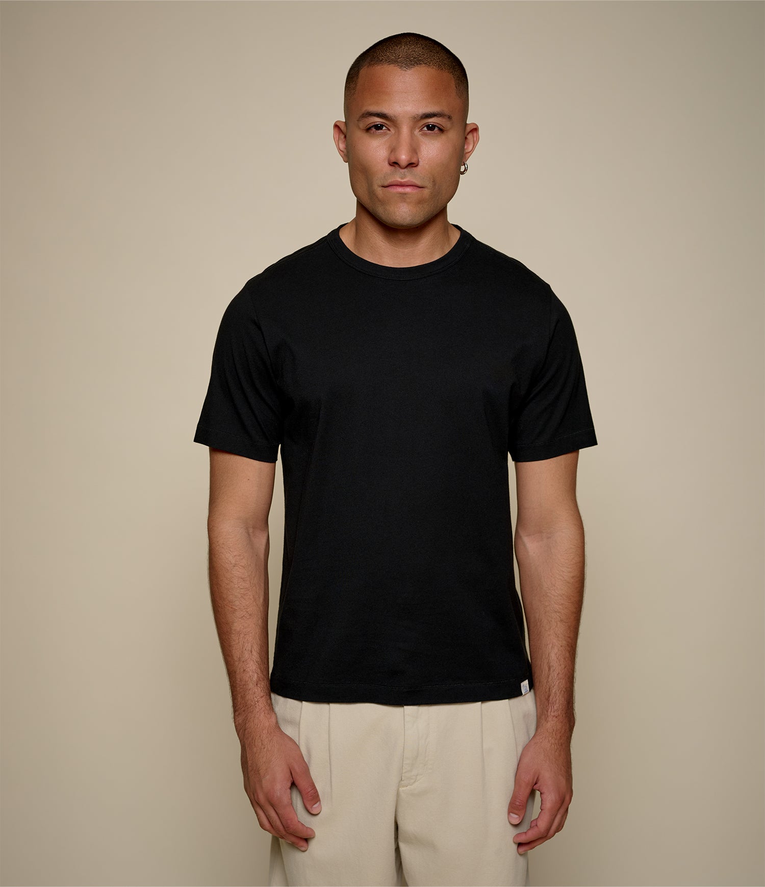 Man wearing a black pima cotton t-shirt and beige pants against a beige background
