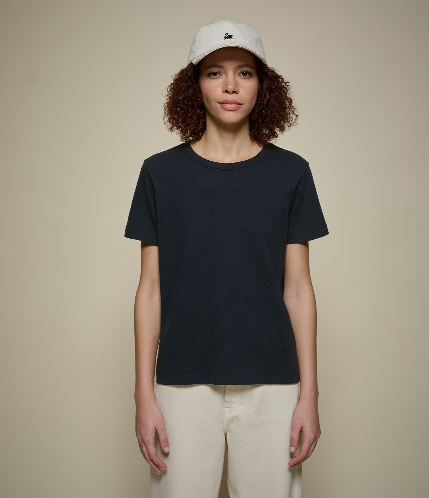 Woman wearing a black t-shirt and white cap on a beige background