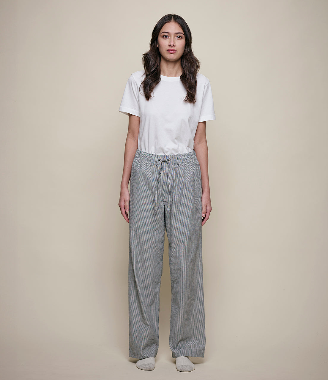 Woman wearing a white t-shirt and gray pants against a beige background