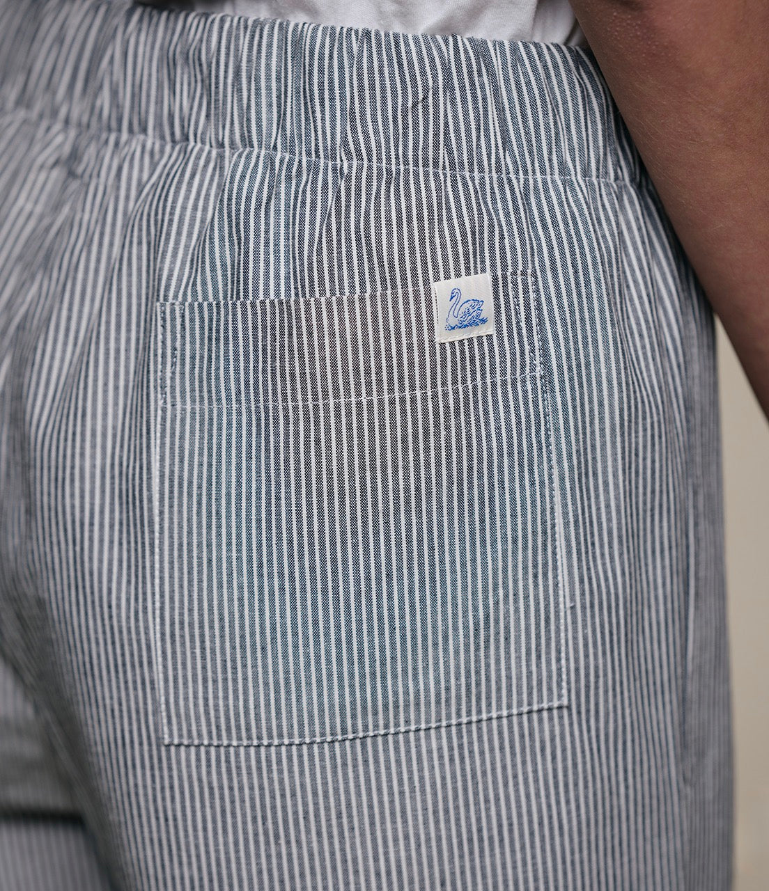 Close-up of gray striped pants with a brand logo on the pocket against a neutral background