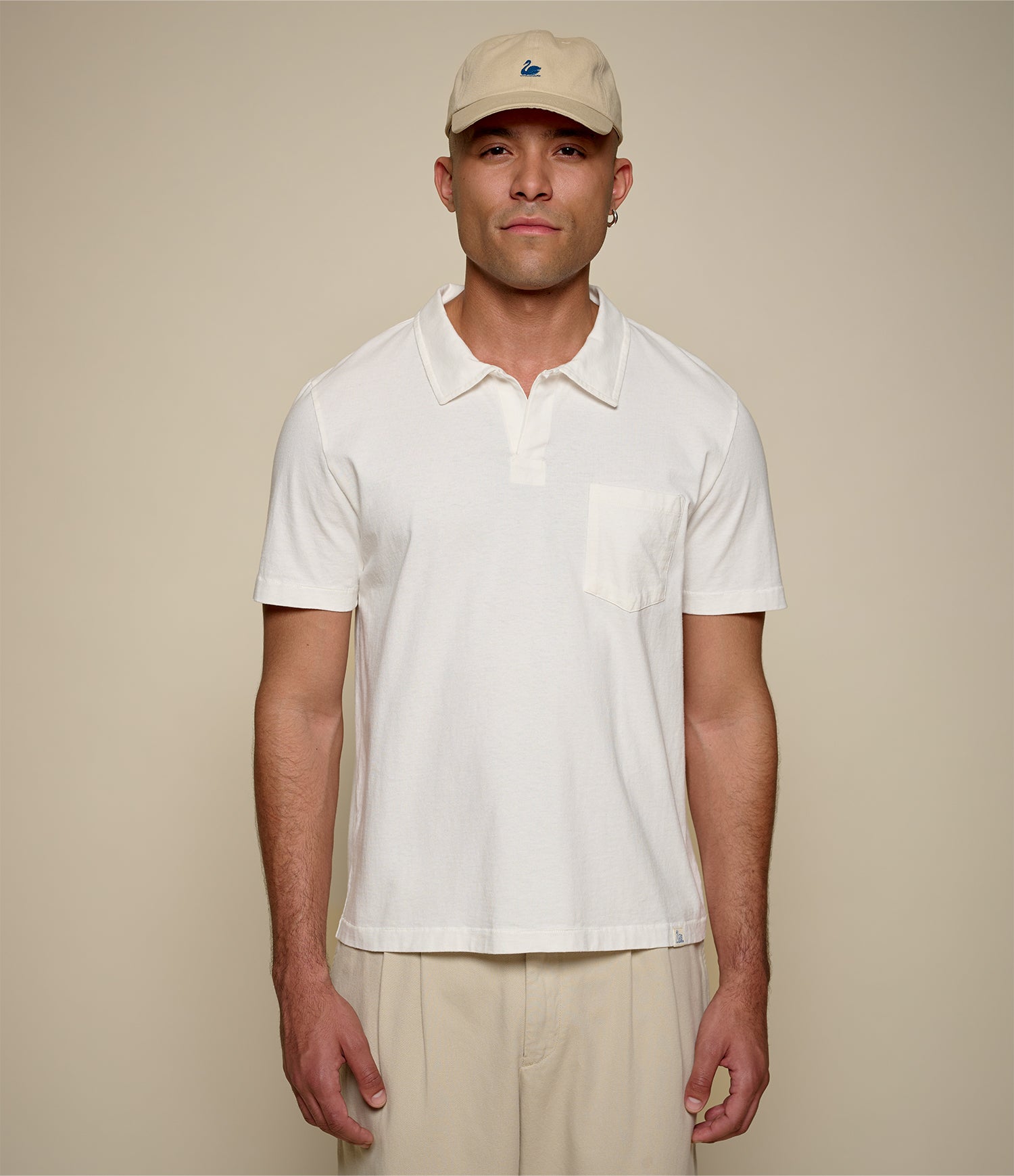 Man wearing a white cotton polo shirt and beige cap against a plain background