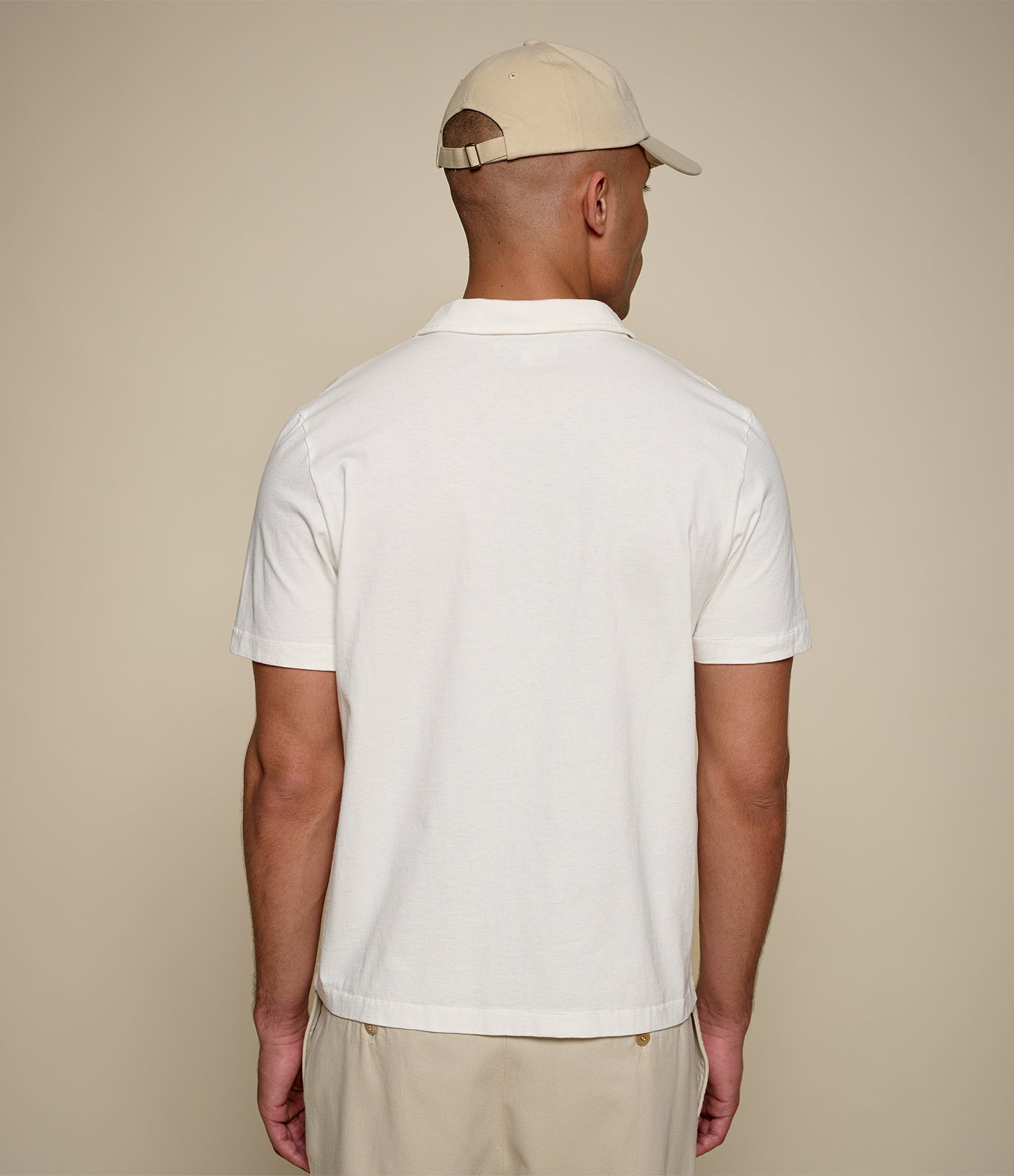 Man wearing a white cotton polo shirt and beige cap against a plain background