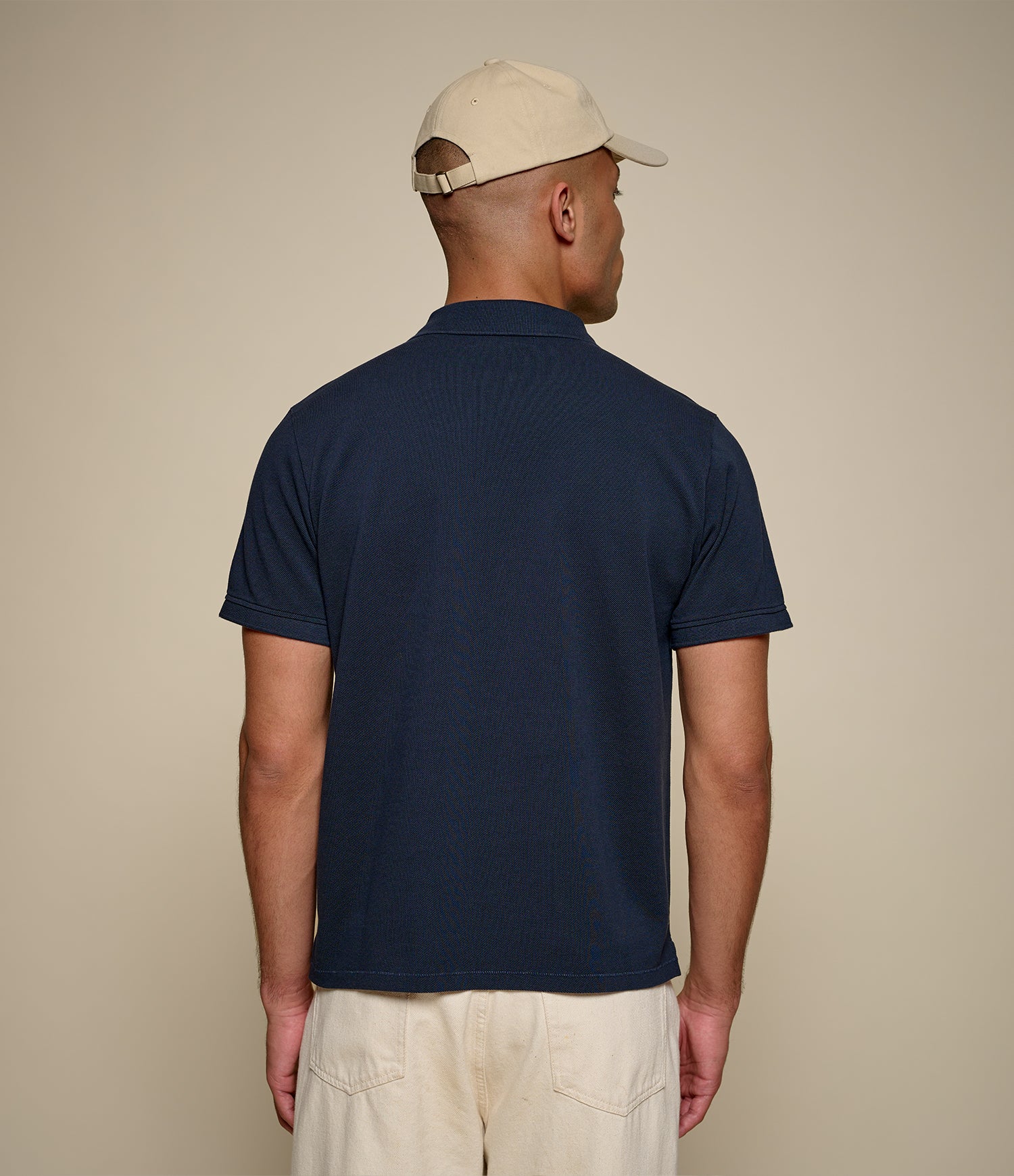Man wearing a navy blue polo shirt and beige cap on a beige background