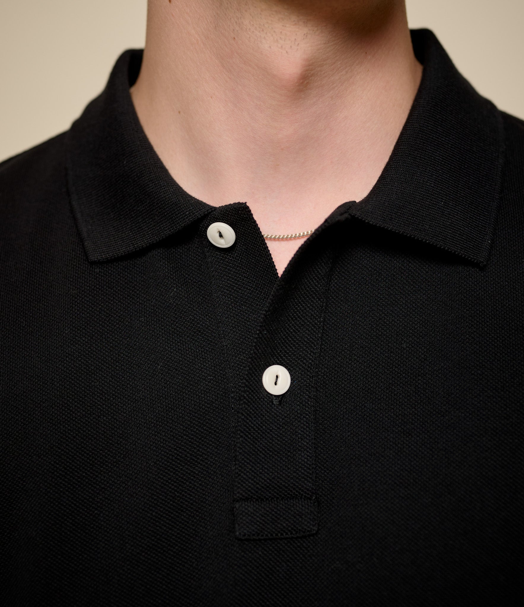 Close-up of a person wearing a black polo shirt with white buttons.