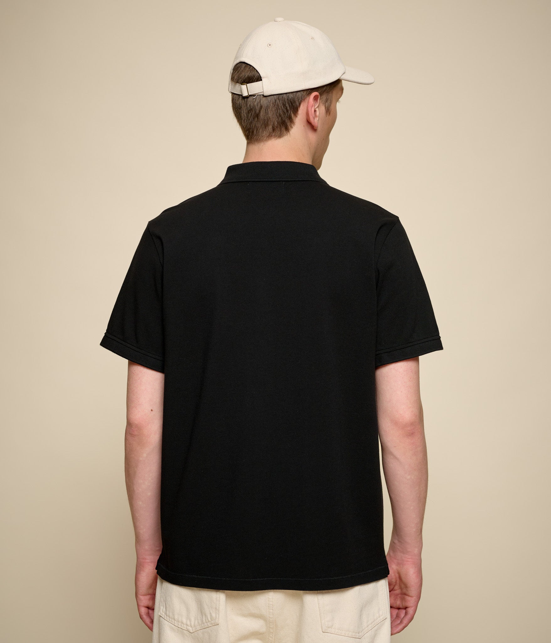 Person wearing a black polo shirt and beige cap on a beige background