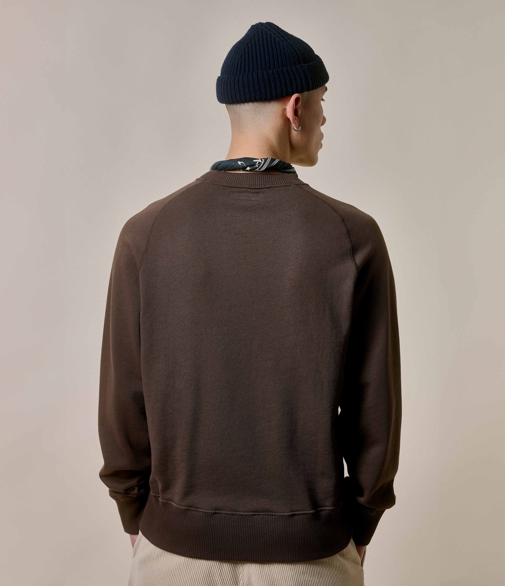 Person wearing a brown jacket and black beanie on a beige background