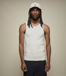 Person wearing a beige tank top and black pants with a plain background