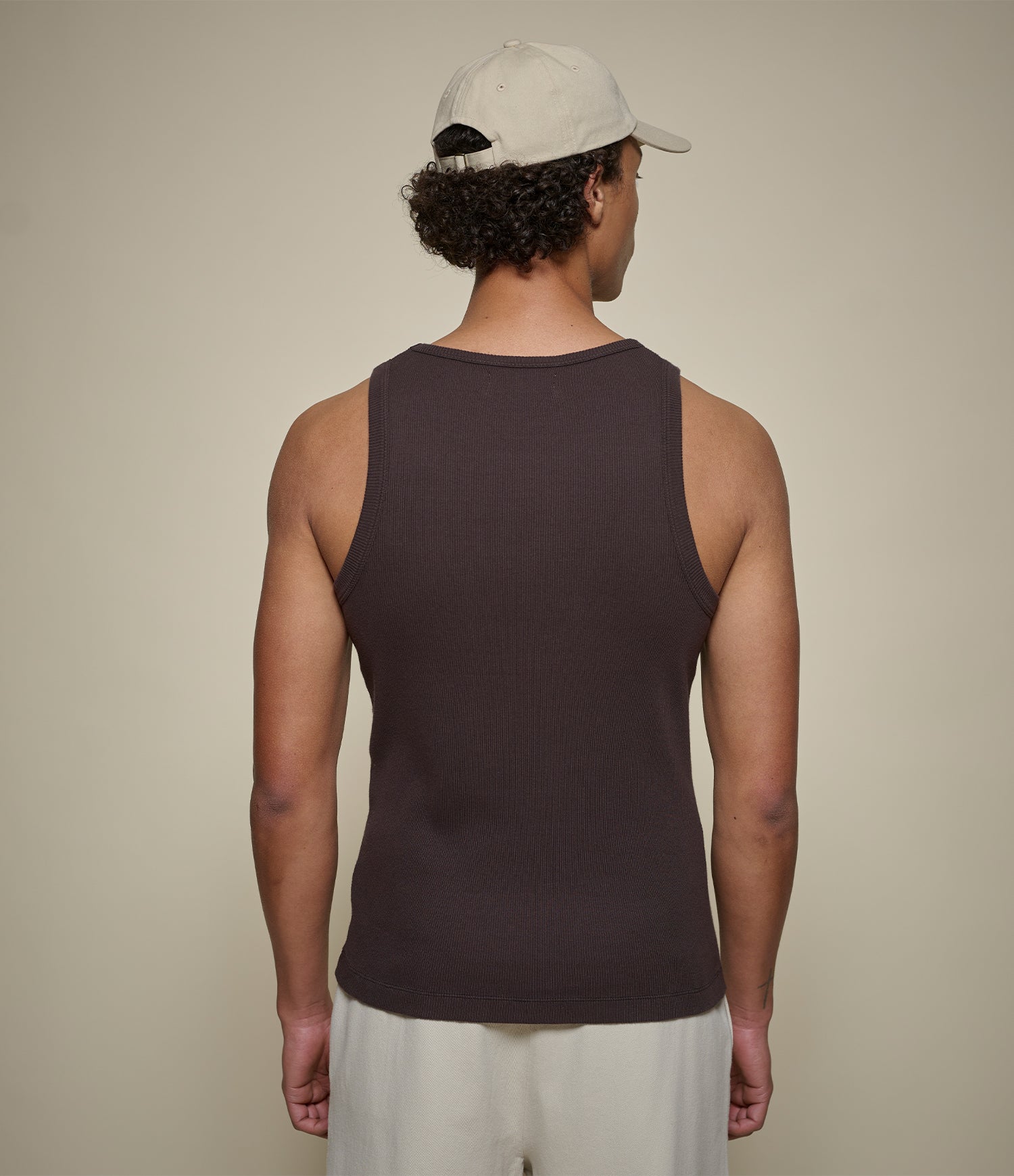 Man wearing brown ribbed tanktop and beige cap