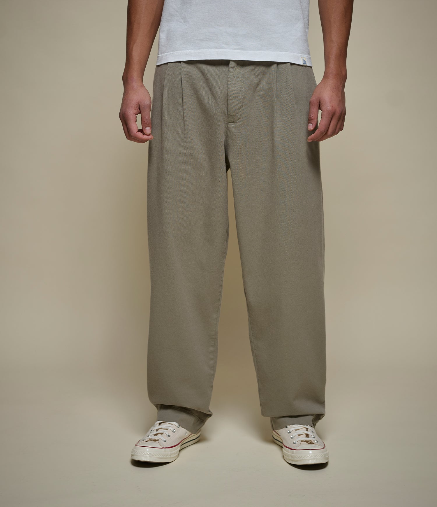 Person wearing green pleated pants and white sneakers on a plain background