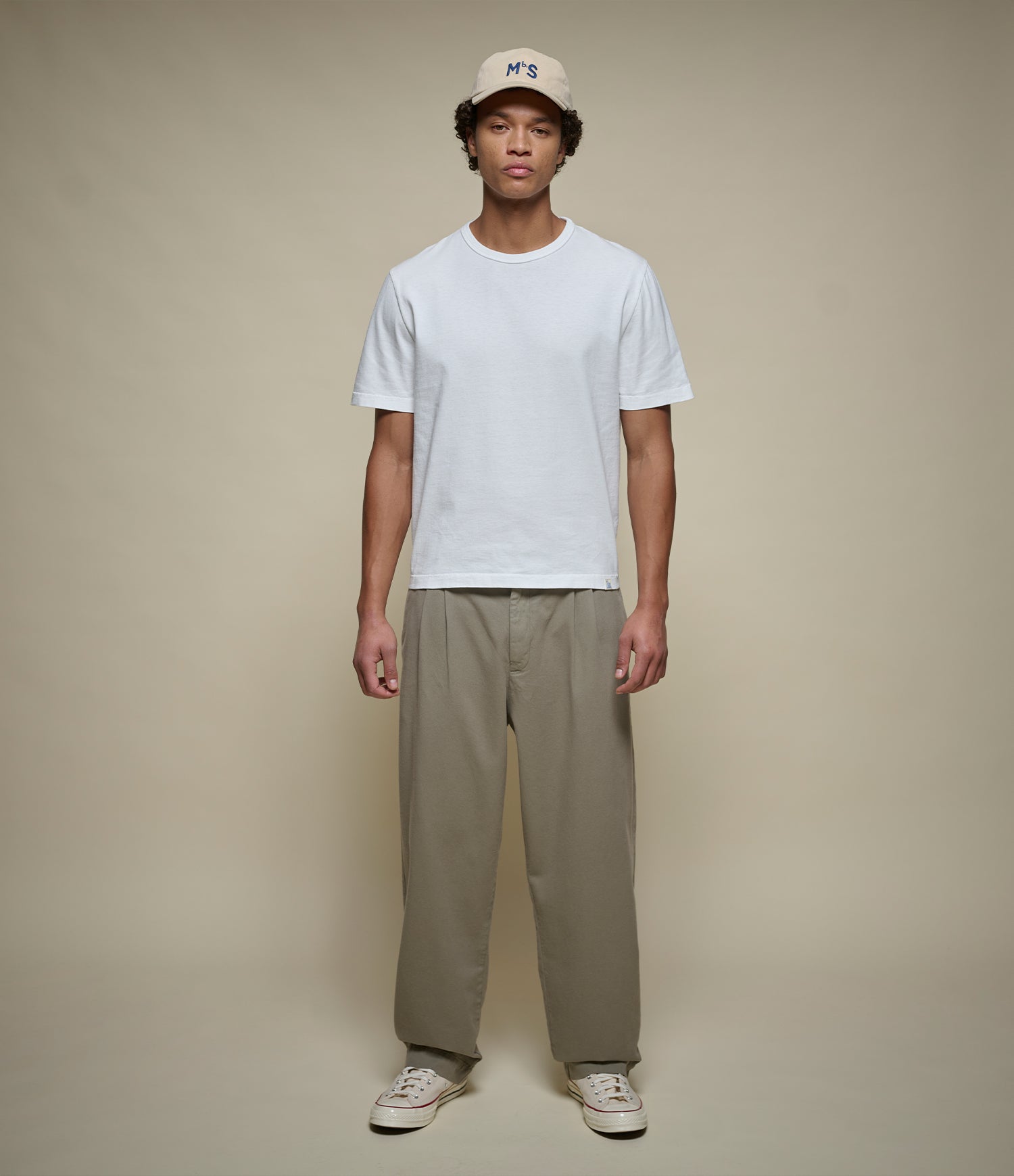Person wearing a white t-shirt, green pants, and a cap on a beige background