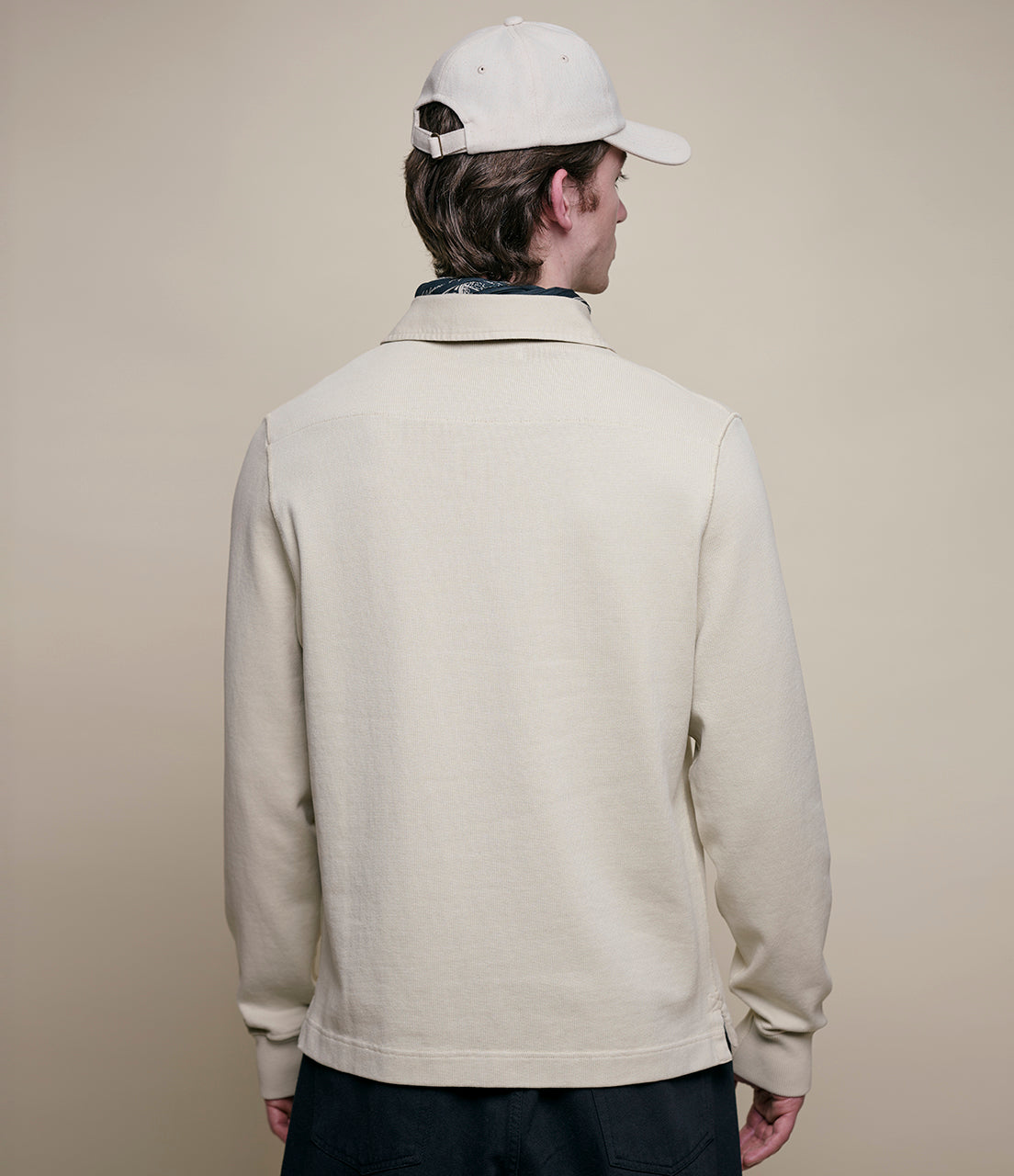 Person wearing a beige rugby shirt and white cap on a plain background