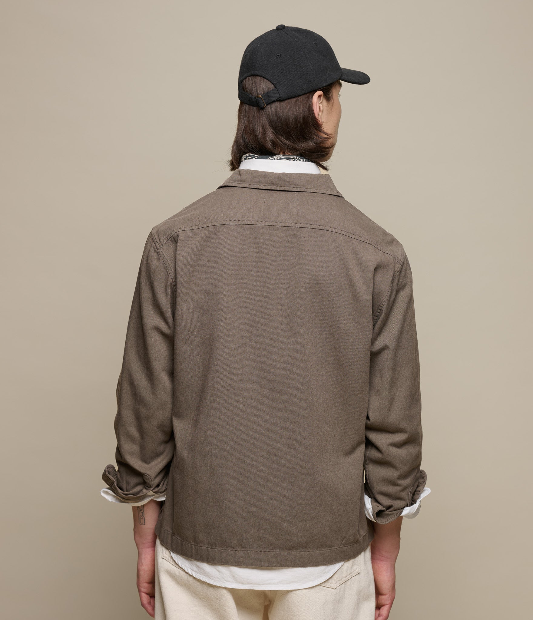 Person wearing a brown jacket and black cap on a beige background