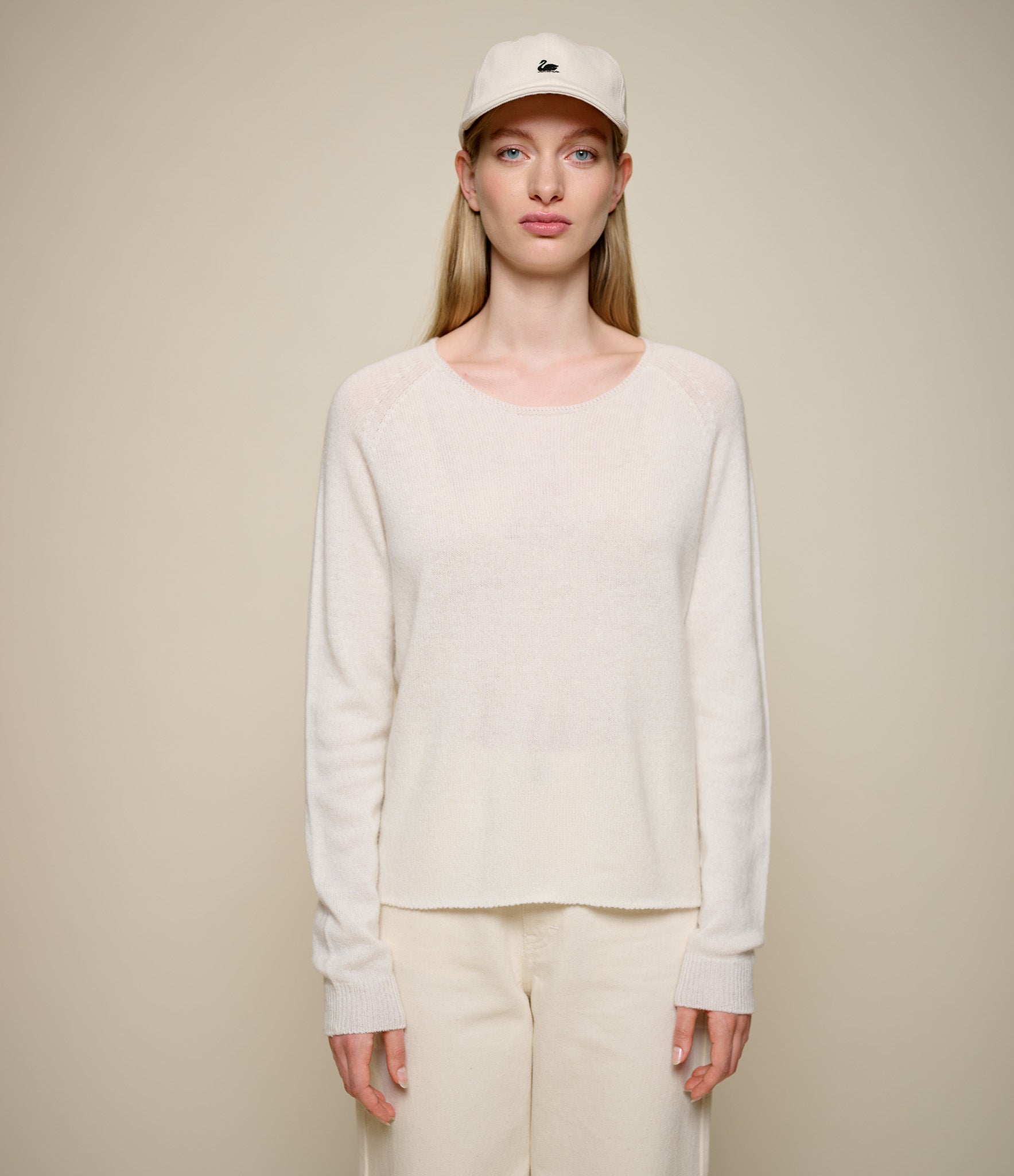 Person wearing a beige lightweight sweater and pants with a cap on a beige background