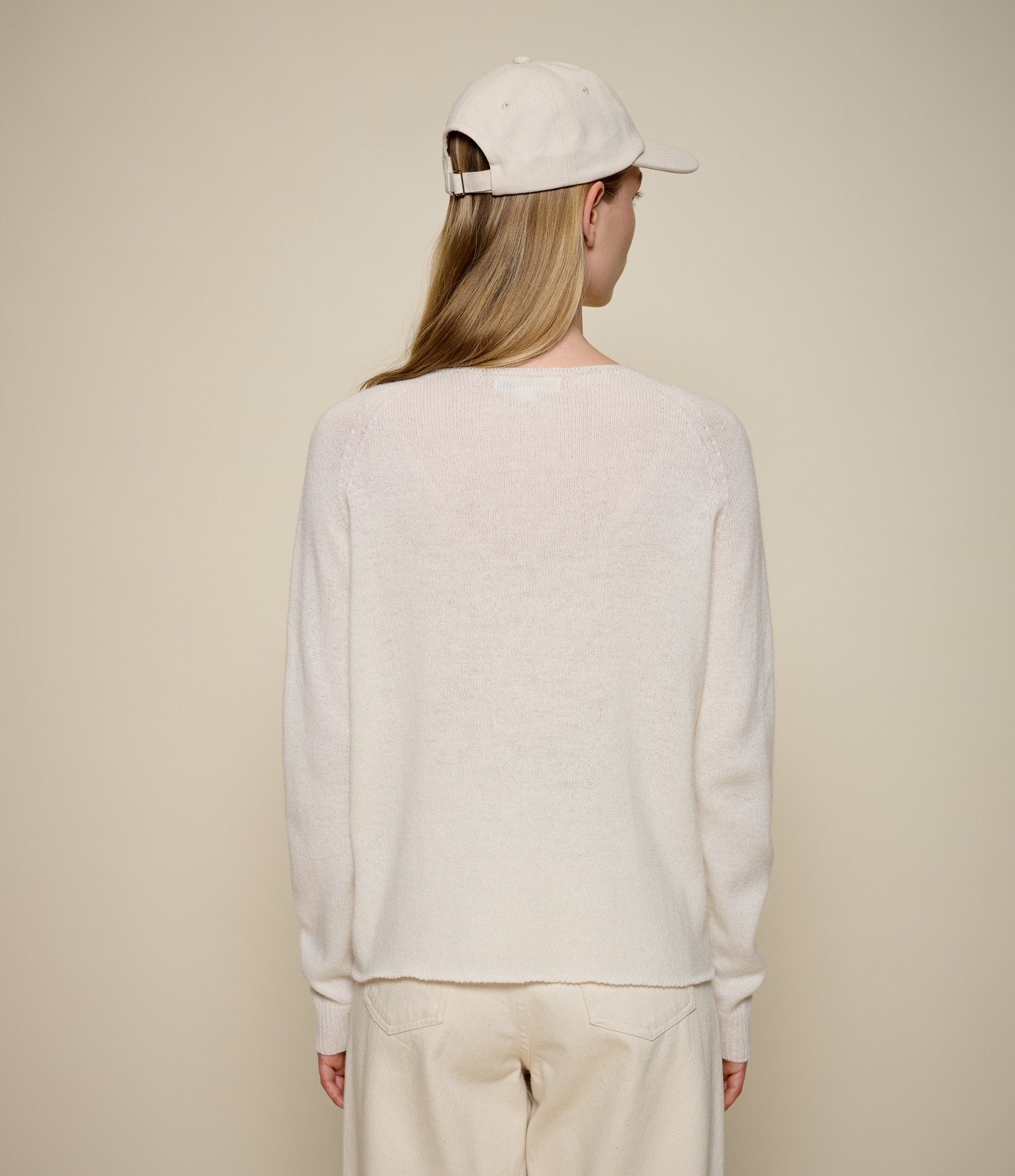 Person wearing a beige lightweight sweater and cap against a beige background