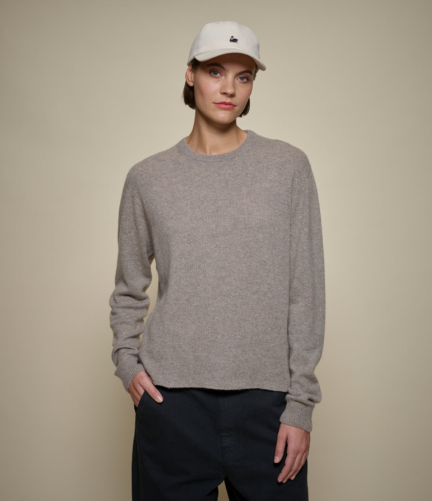 Person wearing a gray sweater and white cap against a beige background