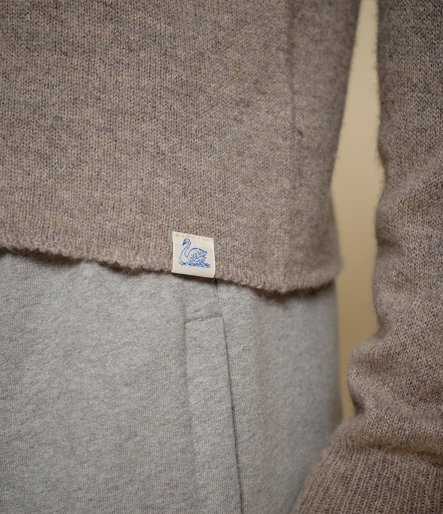 Close-up of a brown sweater with a Merz b. Schwanen brand label on a light gray background