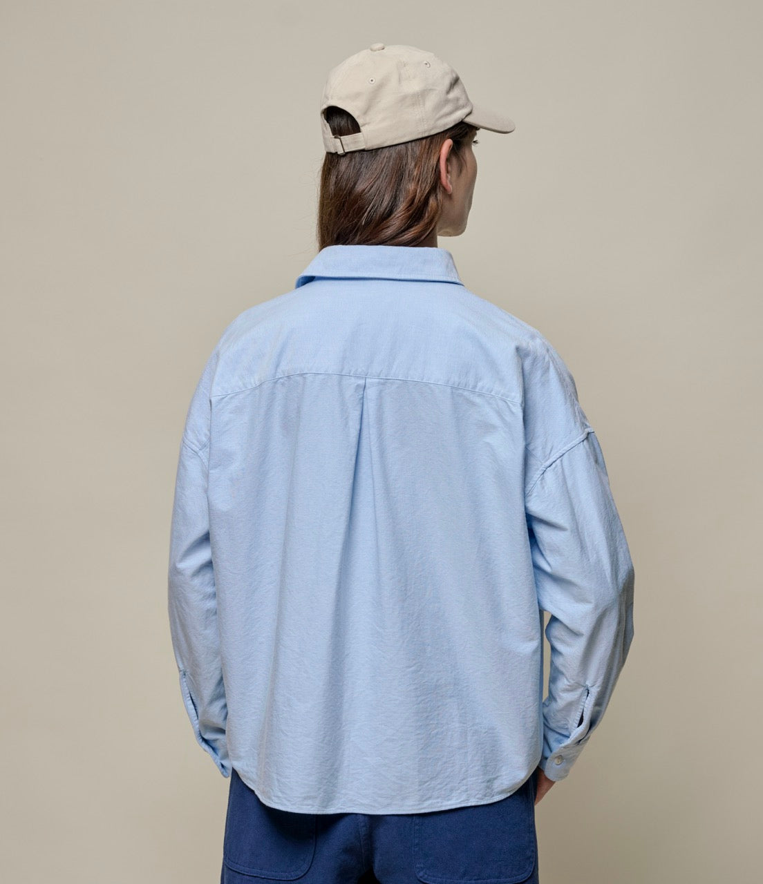 Woman wearing a blue cropped oxford shirt and a beige cap.