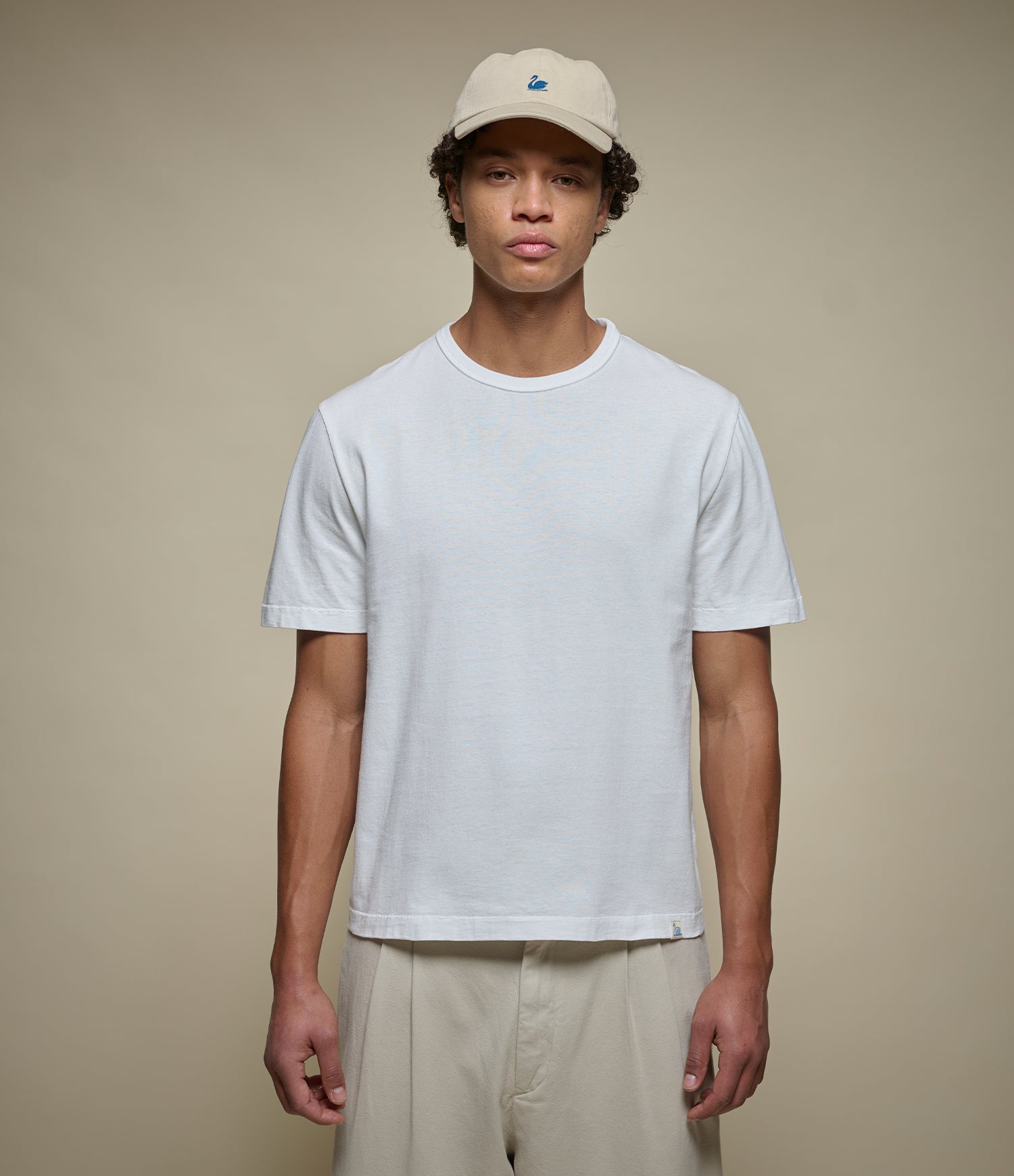 Person wearing a cropped white t-shirt and beige cap against a plain background