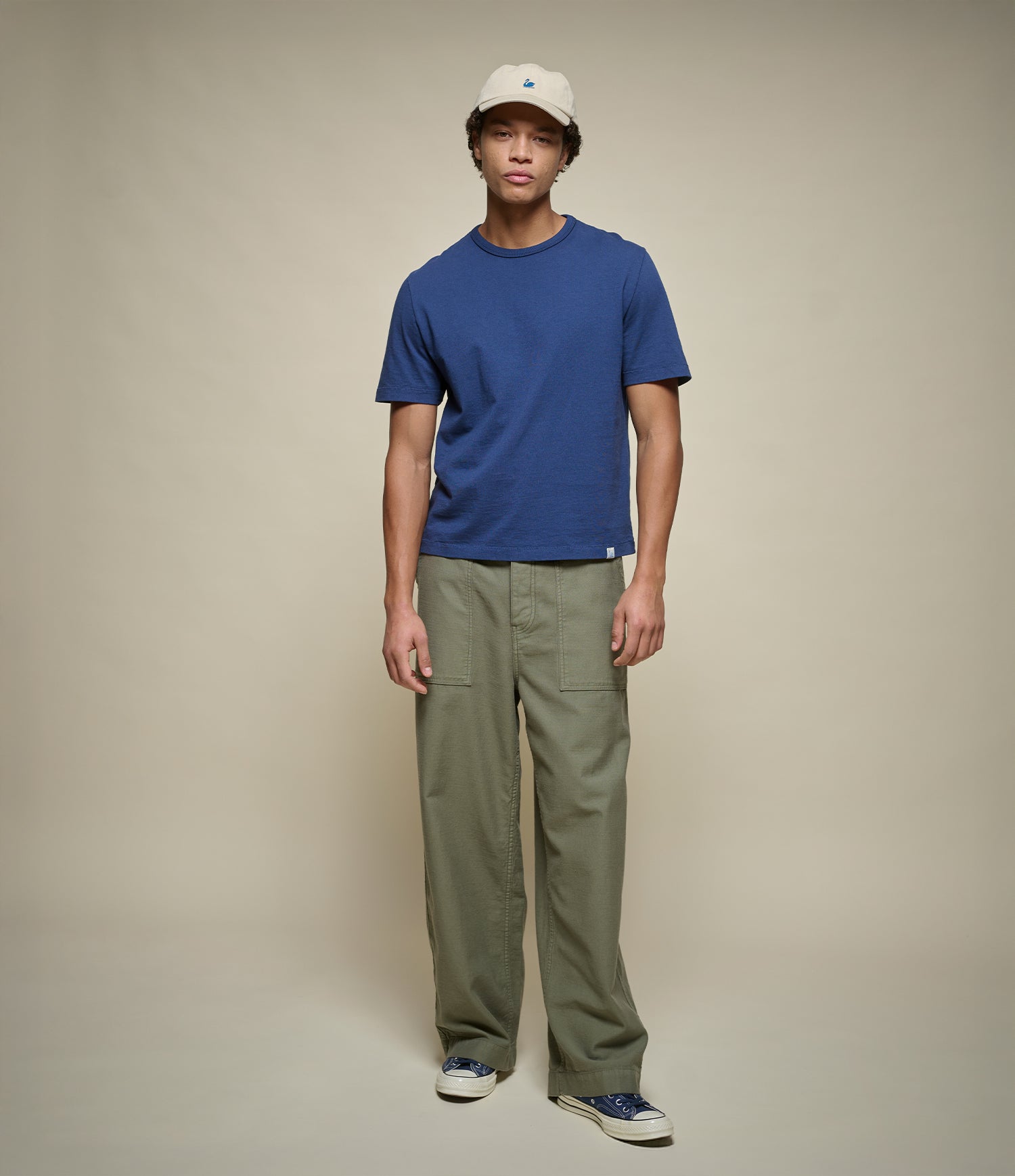 Man wearing a cropped blue t-shirt and green fatigue pants on a beige background