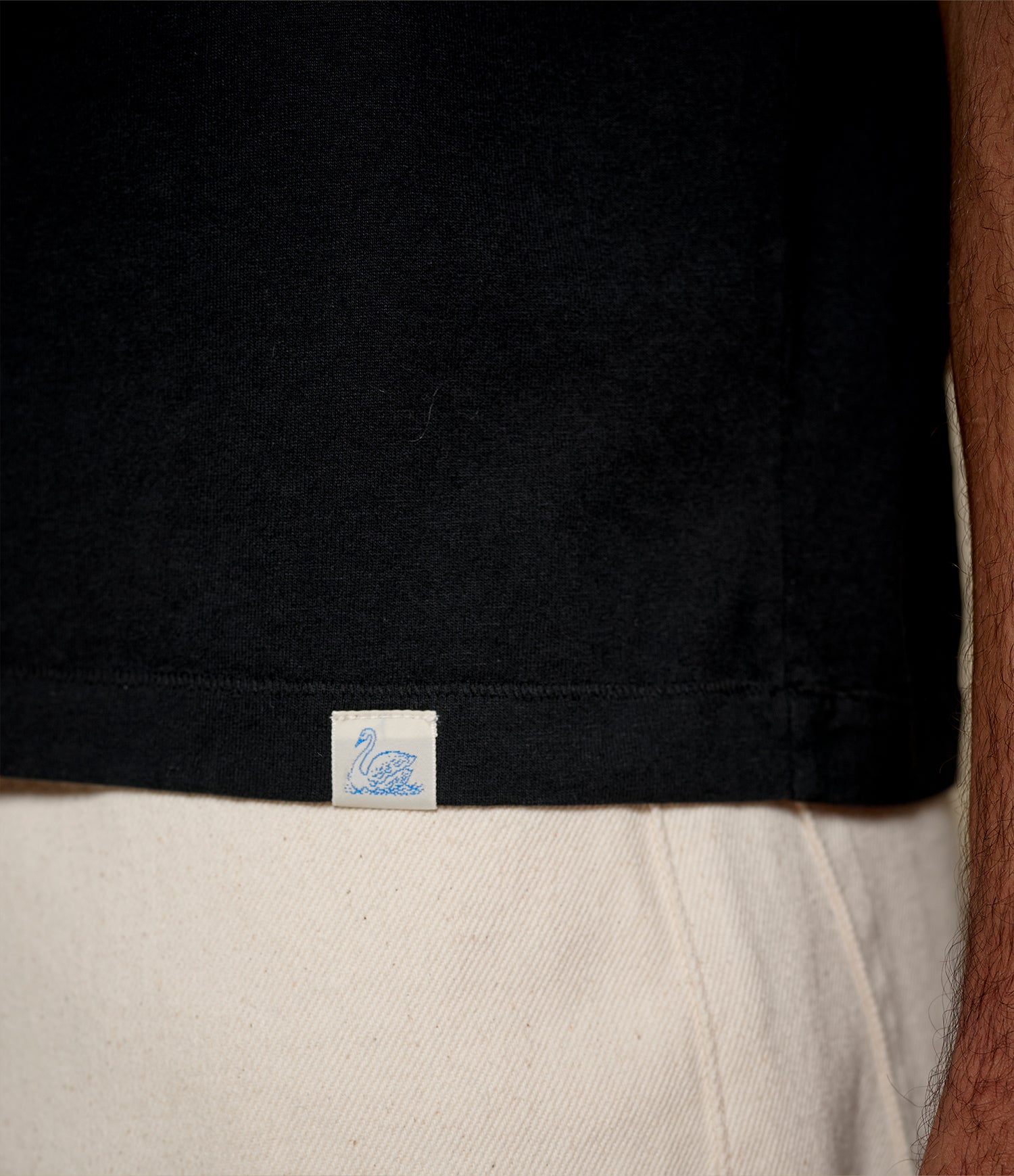 Close-up of black cropped cotton T-shirt with a loop label with a blue swan on the hem.