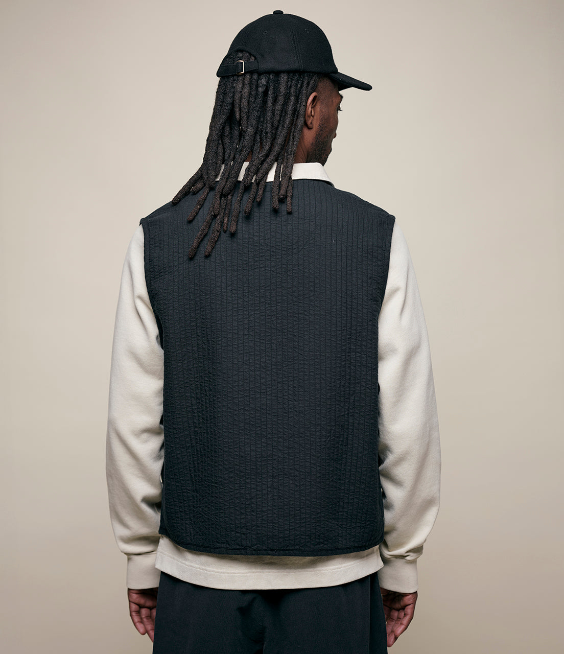 Person wearing a dark vest over a light-colored shirt with a plain background