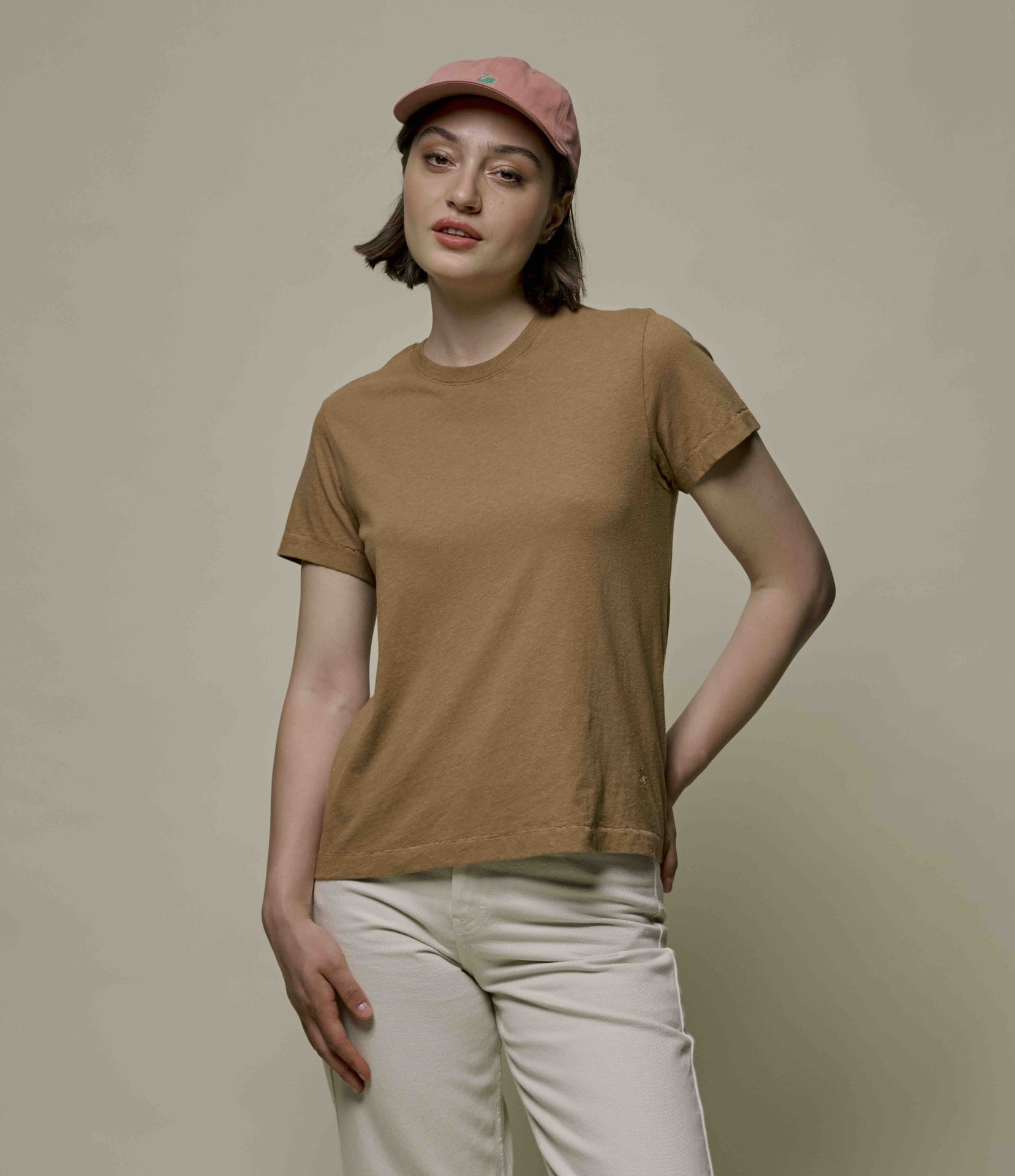 Woman wearing a brown hemp-cotton t-shirt and beige cap against a plain background