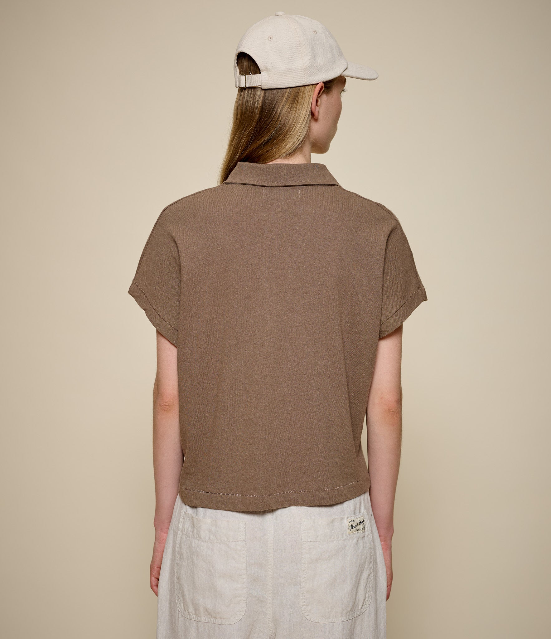 Person wearing a brown linen polo shirt and beige cap on a beige background