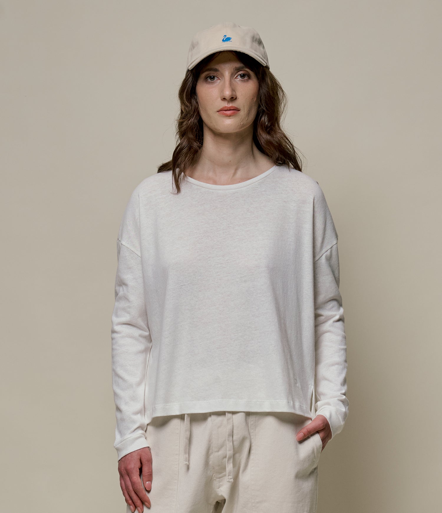 Person wearing a white linen long-sleeve shirt and beige cap against a plain background