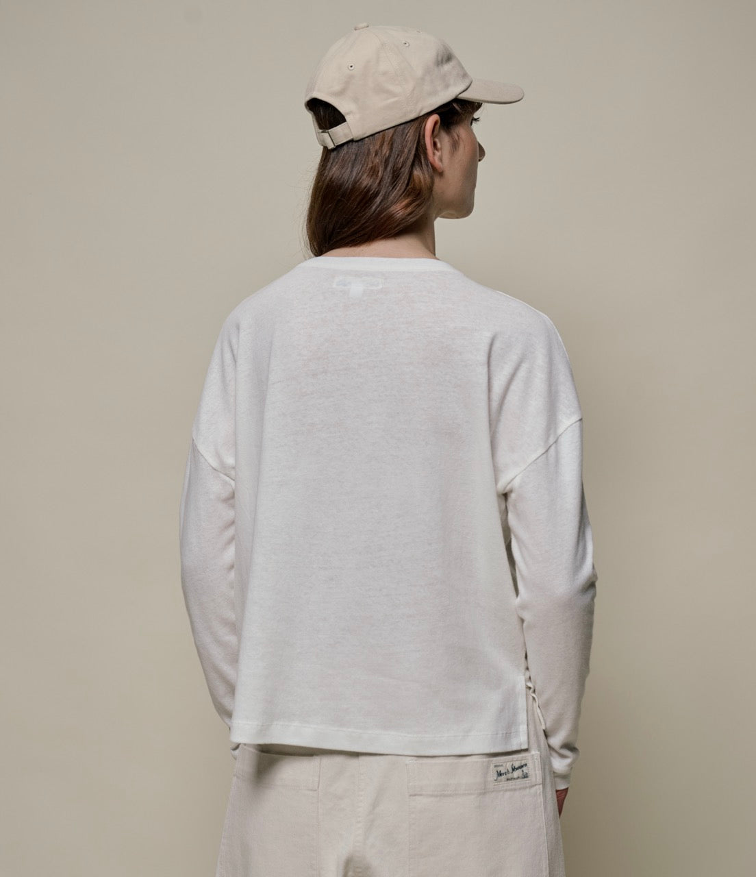 Person wearing a white linen long-sleeve shirt and beige cap against a plain background