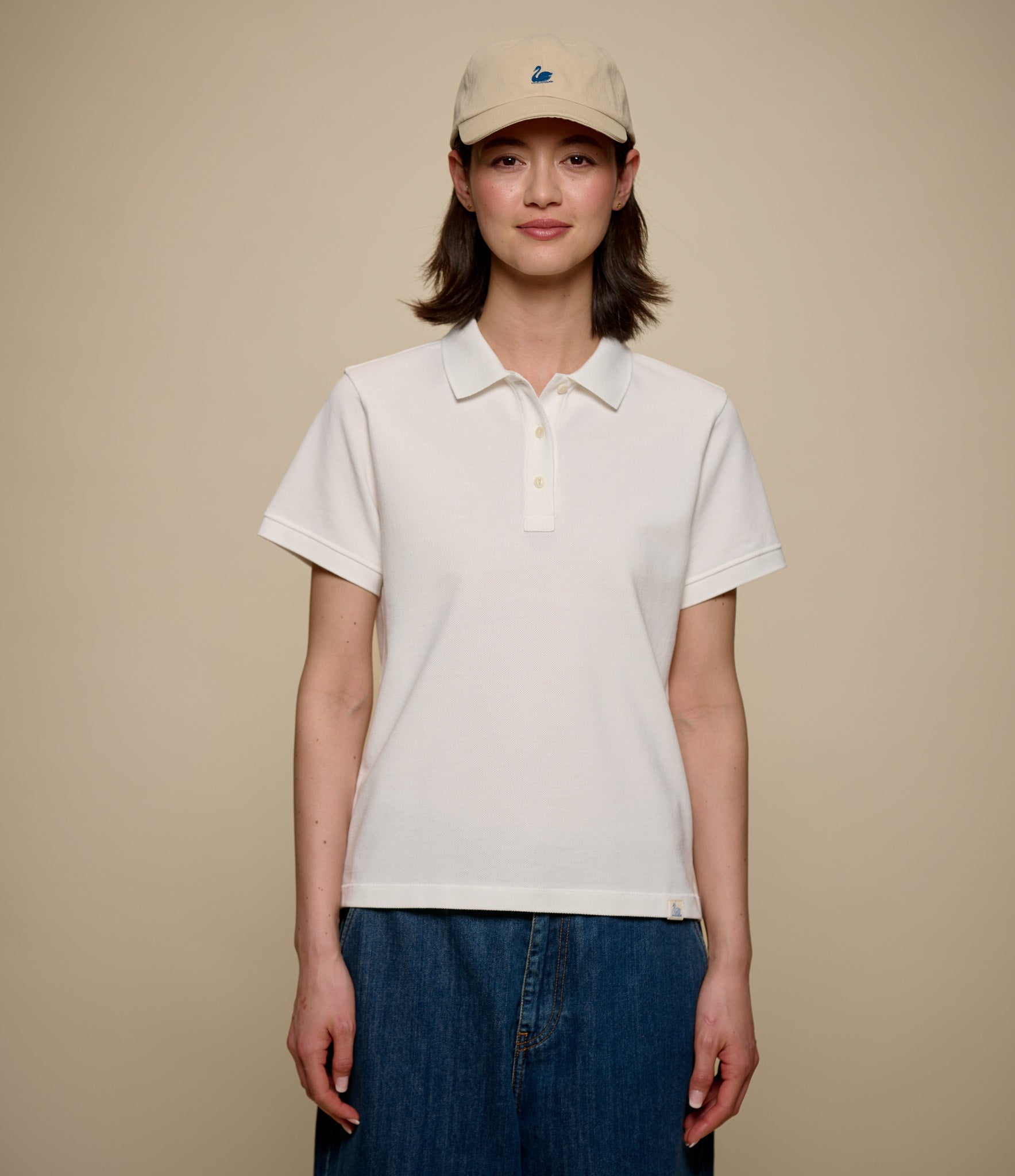Person wearing a white pikée polo shirt and beige cap on a beige background