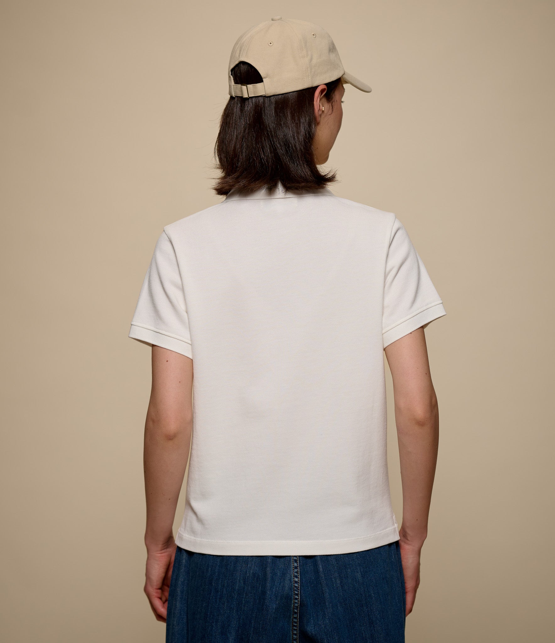 Woman wearing a beige cap and white polo shirt on a beige background