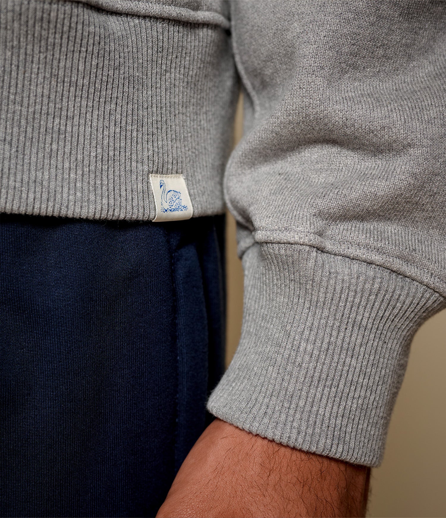 Close-up of gray sweatshirt with a Merz b. Schwanen brand tag on a neutral background